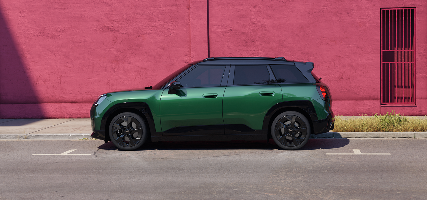 Vista laterale della MINI Aceman 100% elettrica in British Racing Green con tetto nero, parcheggiata in strada.