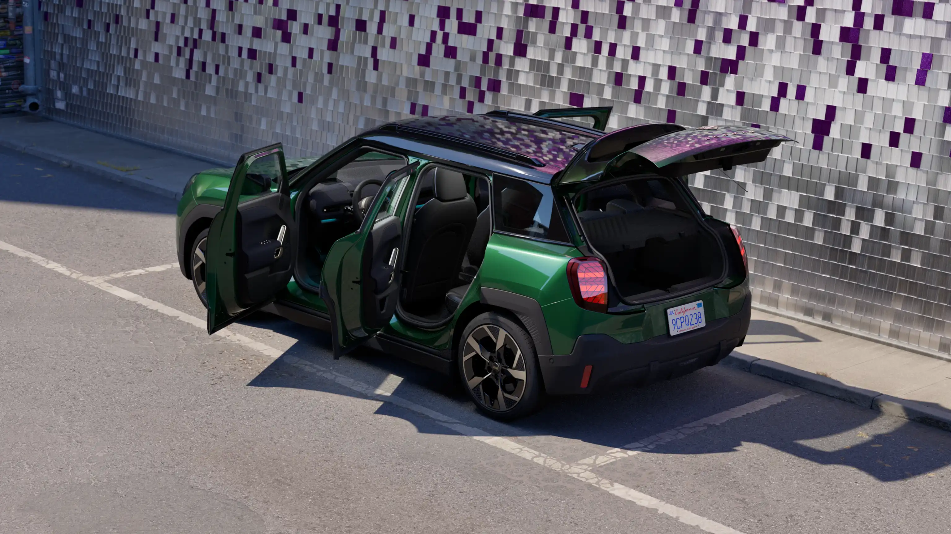 Vista posteriore laterale della MINI Aceman 100% elettrica in British Racing Green parcheggiata in un parcheggio con tutte le porte aperte e un muro colorato sullo sfondo