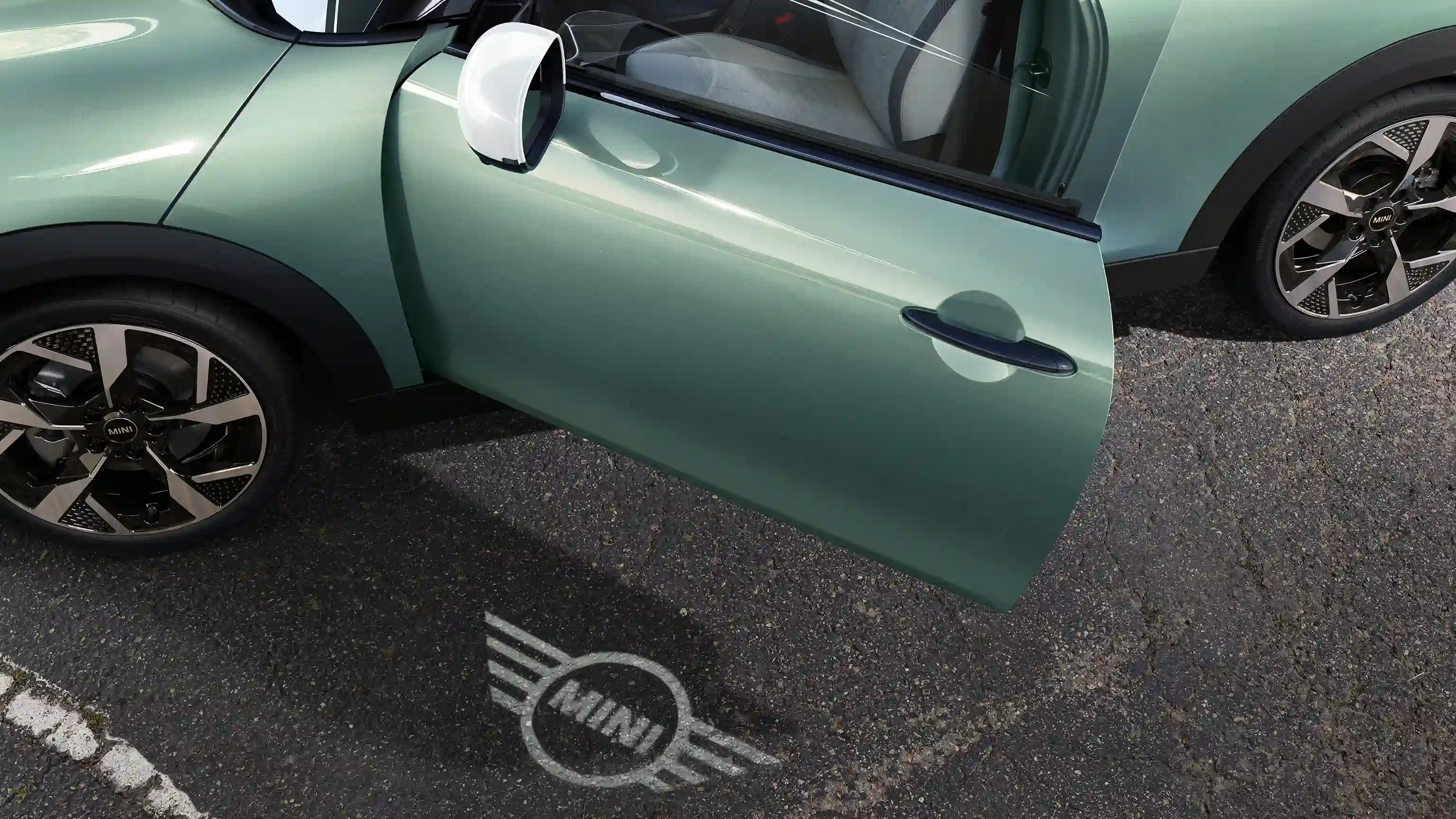 Vista esterna della MINI Cooper con portiera aperta e luce di benvenuto con il logo MINI proiettato sul suolo 