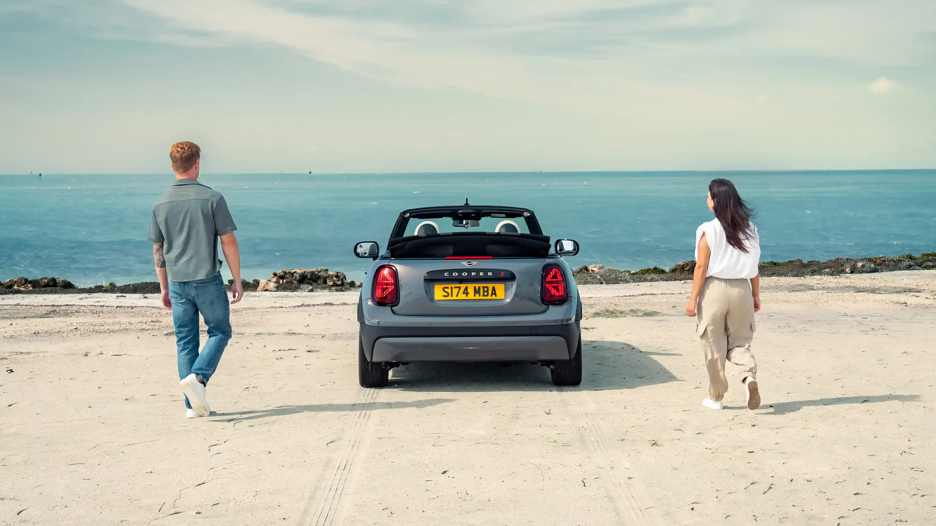 Vista posteriore di una MINI Cooper Cabrio parcheggiata su una spiaggia con due persone