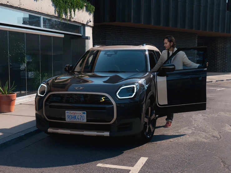Vista frontale di MINI Countryman 100% elettrica in Midnight Black con tetto Vibrant Silver su strada.