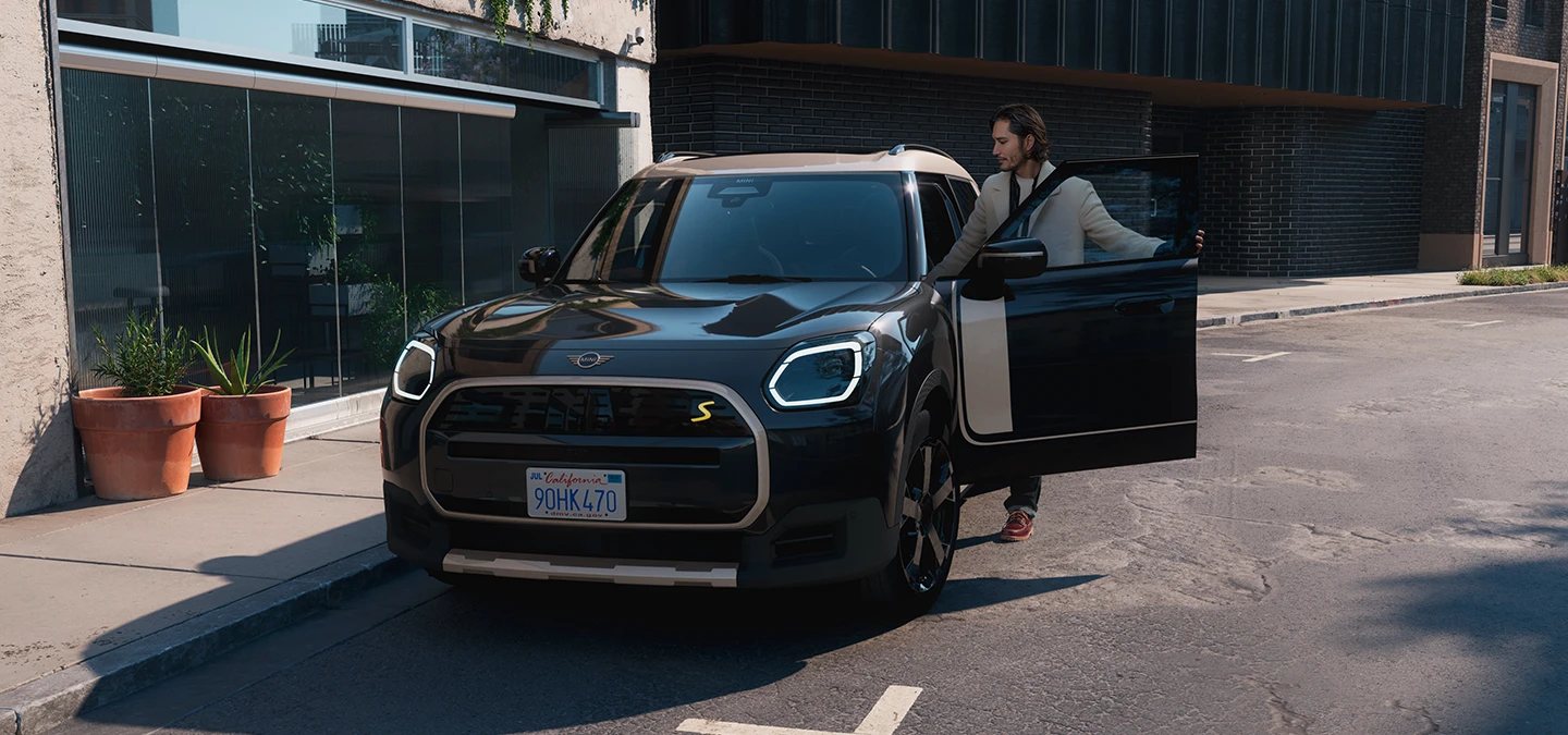 Vista frontale di MINI Countryman 100% elettrica in Midnight Black con tetto Vibrant Silver su strada.
