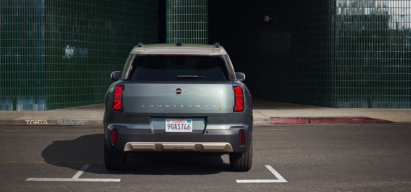 Vista posteriore di MINI Countryman 100% elettrica in Smokey Green con tetto Vibrant Silver parcheggiata. 