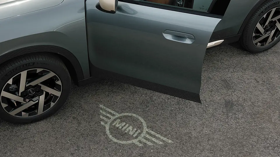 Vista esterna della MINI Countryman con portiera aperta e luce di benvenuto con logo MINI proiettata a terra