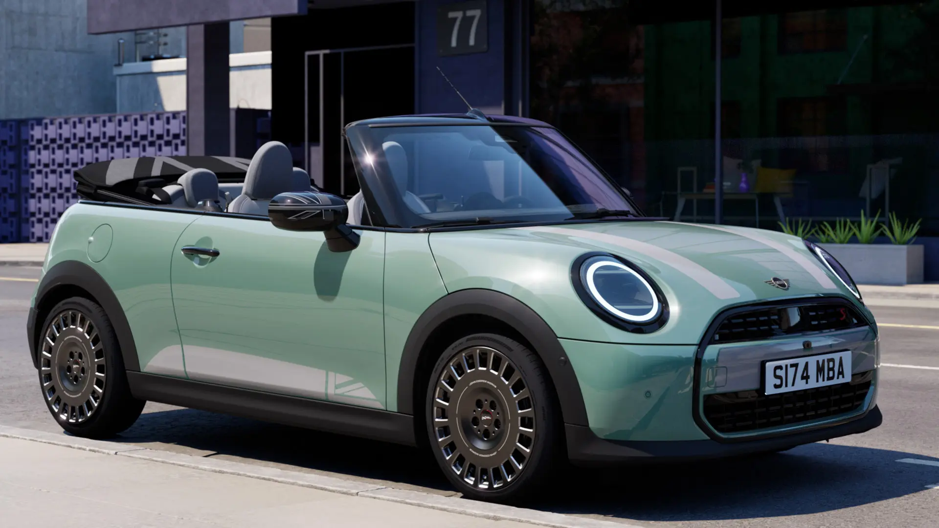 Vista laterale frontale della MINI Cabrio in Ocean Wave Green con decalcomanie per il cofano anteriore MINI Heritage di colore bianco. 