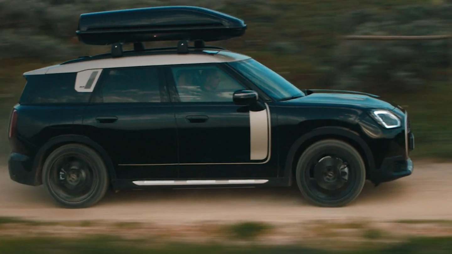 Una MINI Countryman in Midnight Black metallizzato con cerchi John Cooper Works Runway Spoke da 19" in nero su una strada sterrata.
