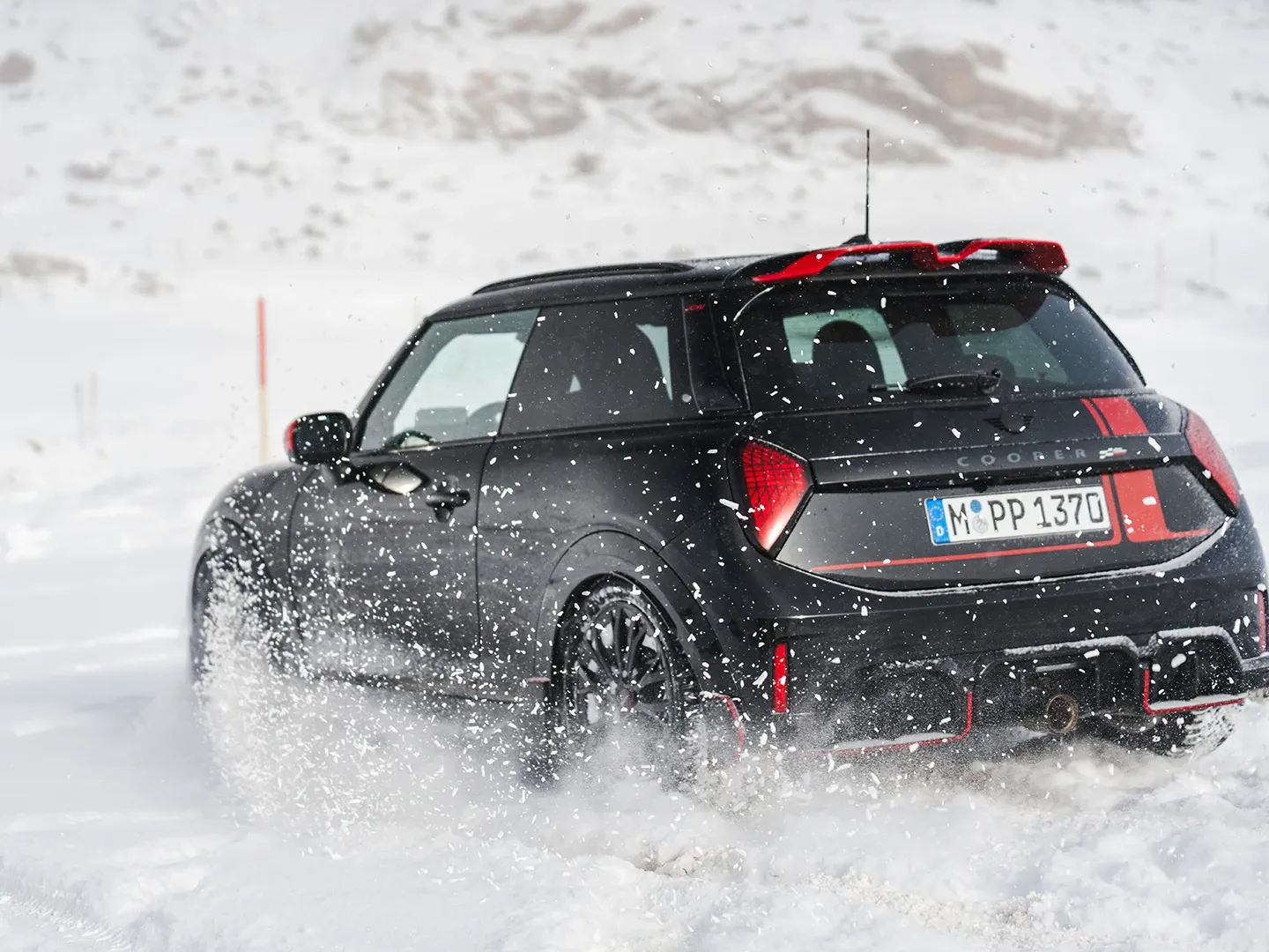 Vista posteriore di una MINI Cooper JCW in movimento sulla neve.