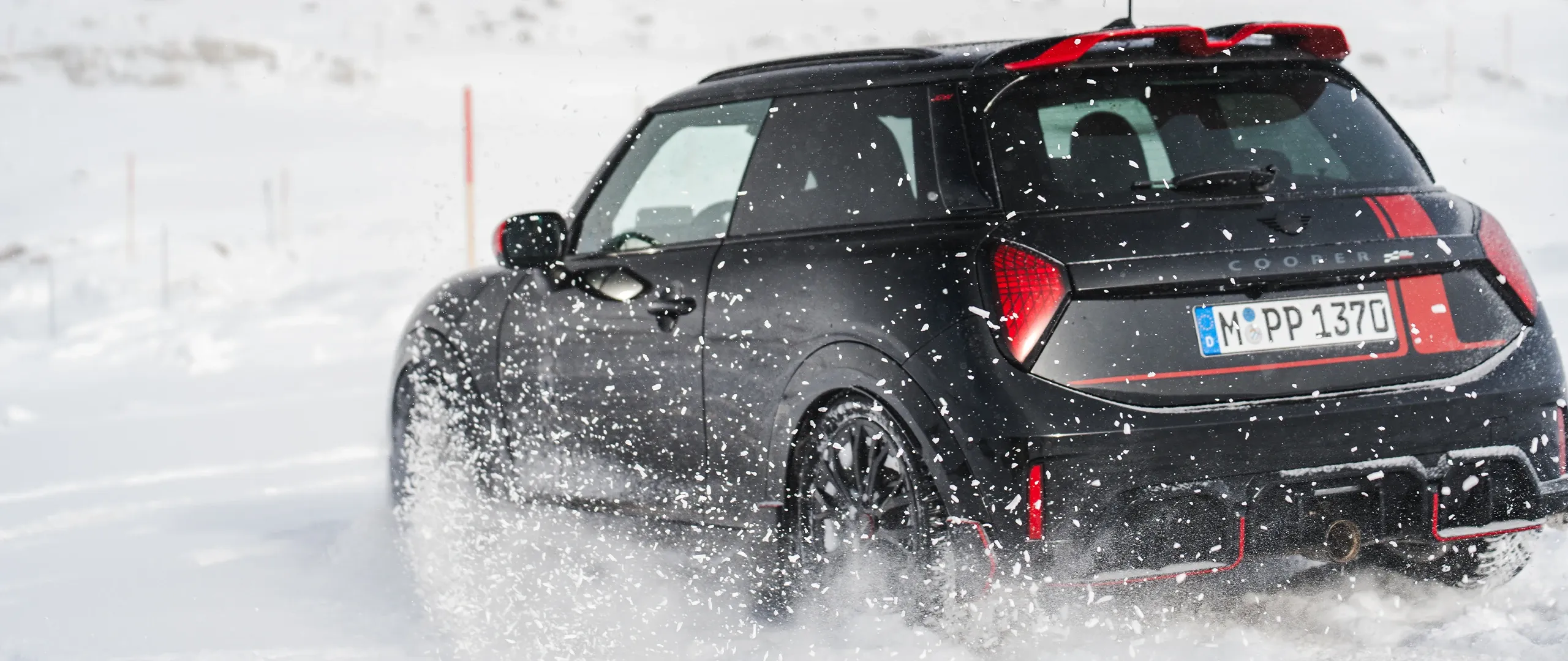 Vista posteriore di una MINI Cooper JCW in movimento sulla neve.