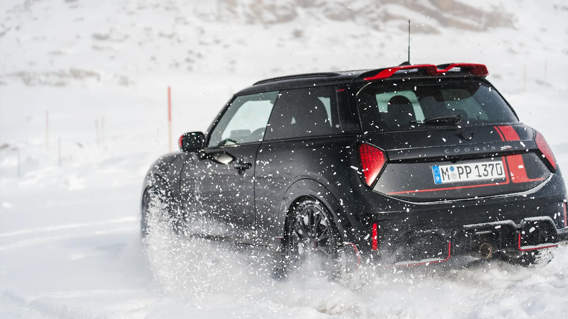 Vista posteriore di una MINI Cooper JCW in movimento sulla neve.