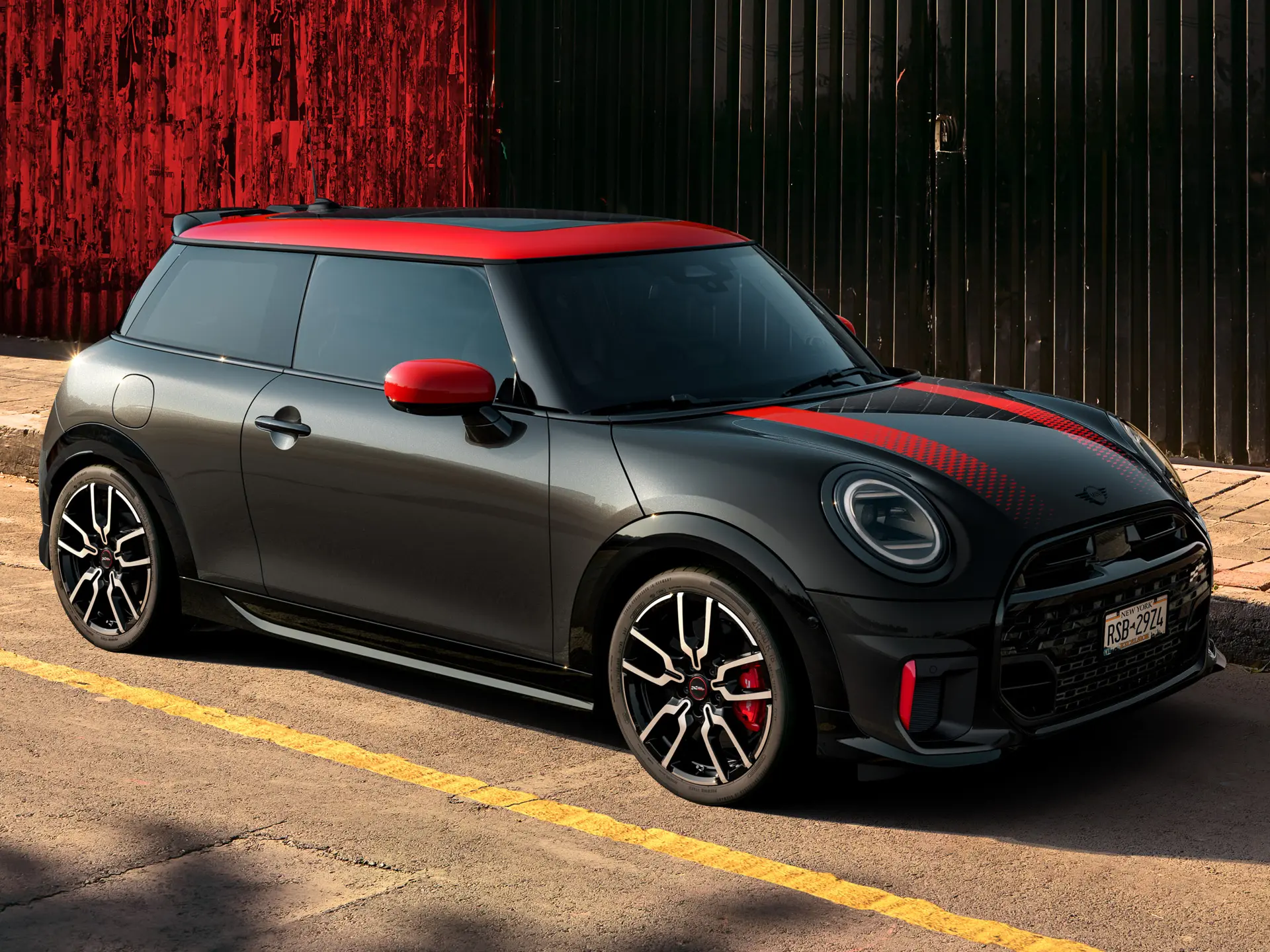 MINI John Cooper Works a 3 porte in Midnight Black con tetto e gusci retrovisori in Chili Red e strisce sportive rosse, vista laterale, parcheggiata in strada.