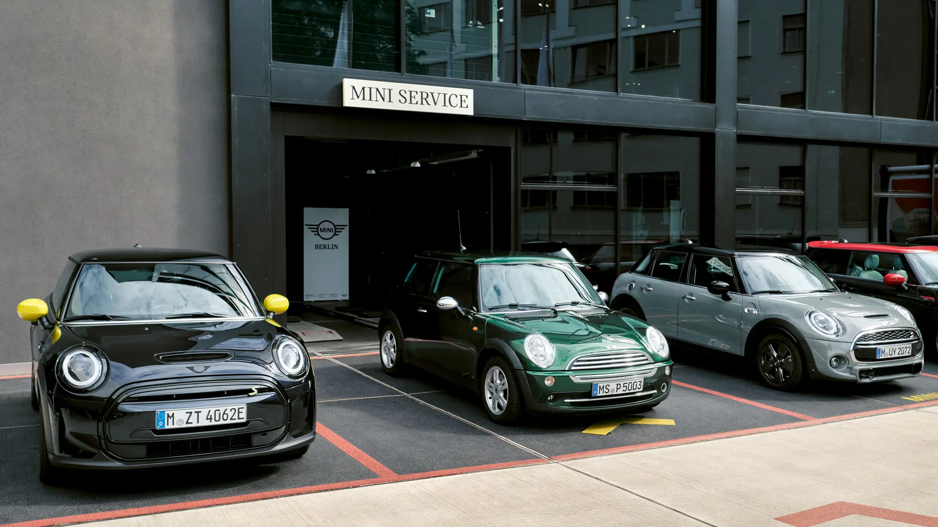 MINI Cooper Electric S in nero all’esterno di un concessionario MINI insieme a una MINI Cooper a 3 porte in verde, MINI a 5 porte in argento, MINI JCW Black, vista anteriore. 