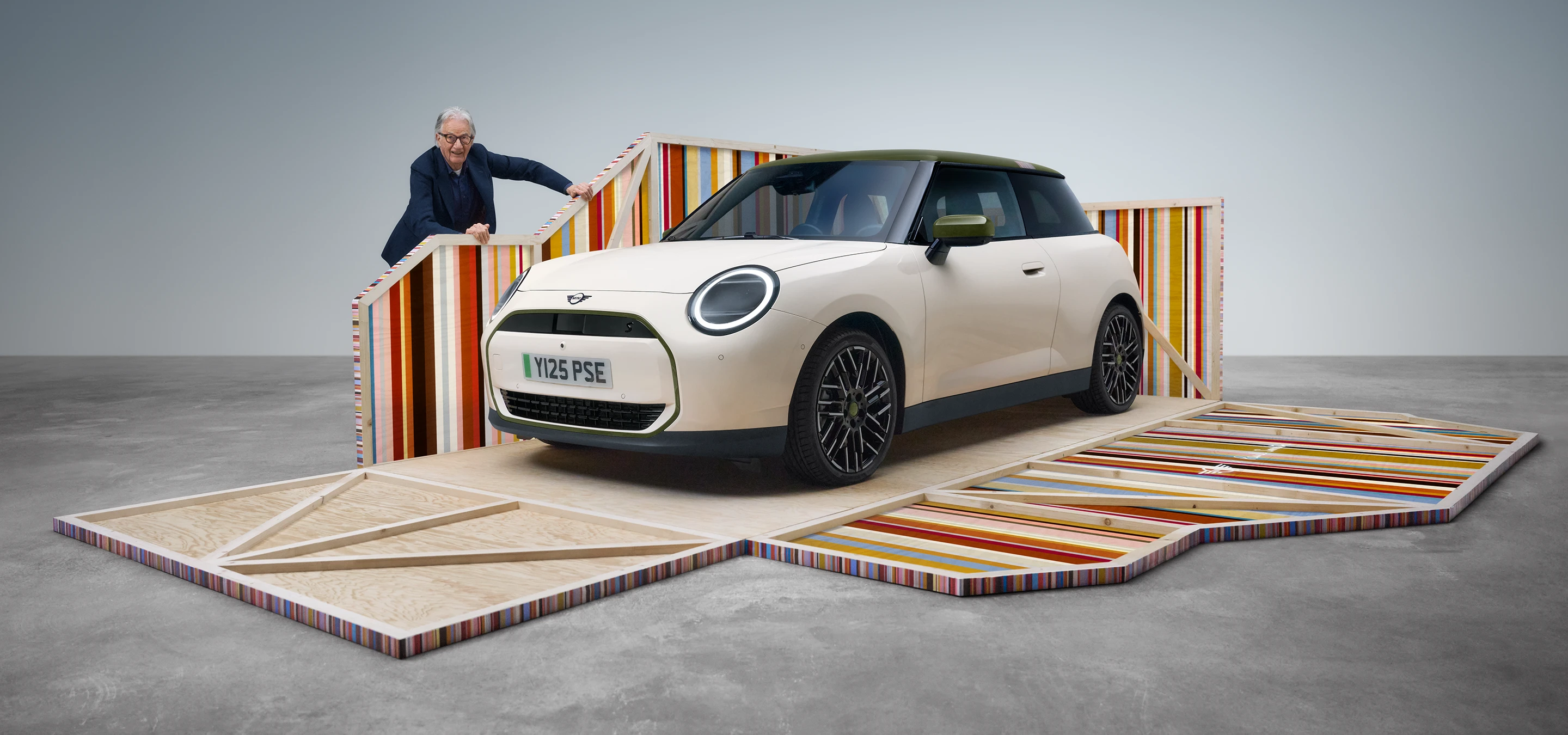Vista laterale della parte anteriore della MINI Cooper Paul Smith Edition 100% elettrica in Inspired White con il designer Paul Smith